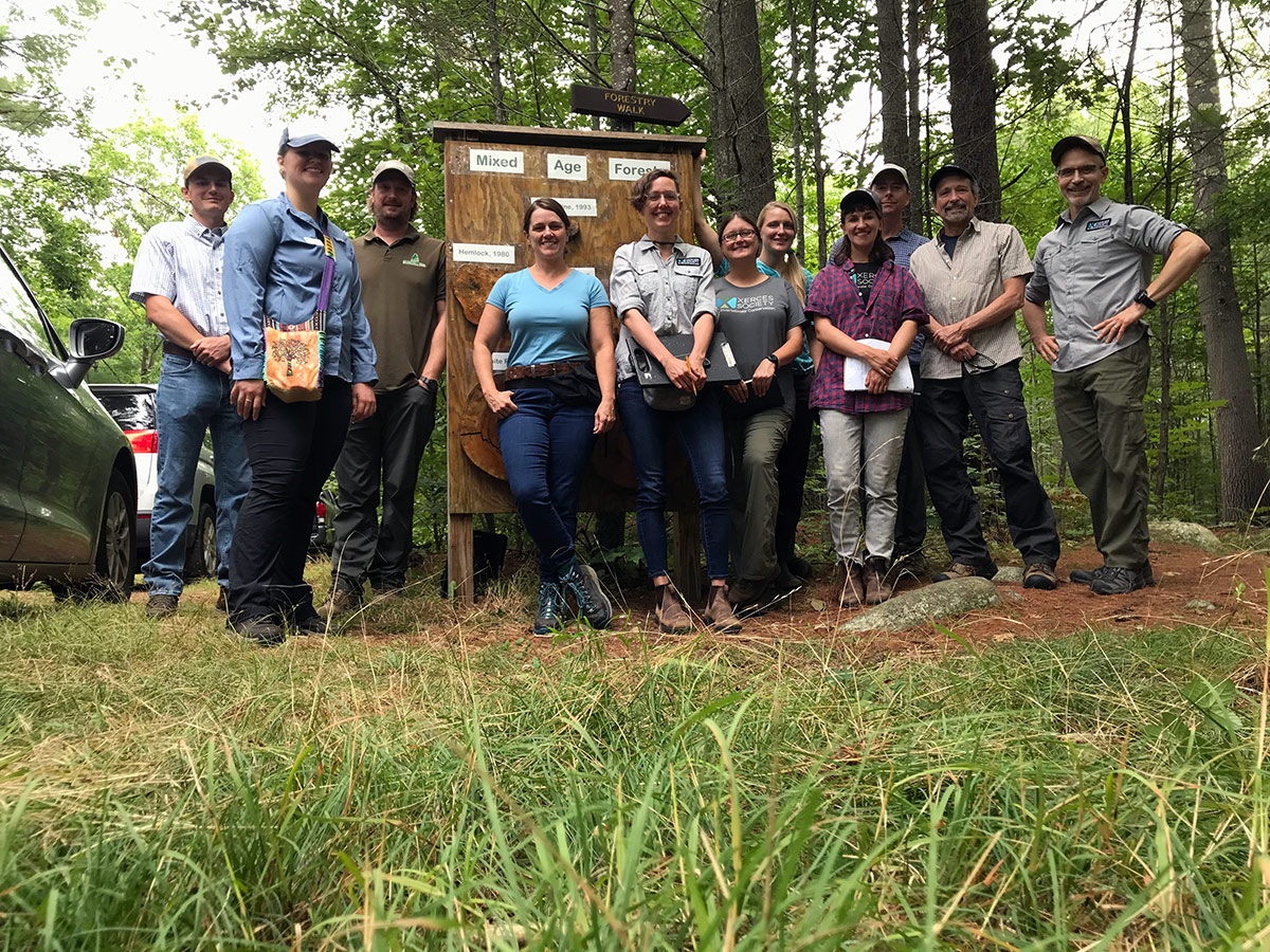 Group of people posing in front of an educational sign near the entrance to the forest