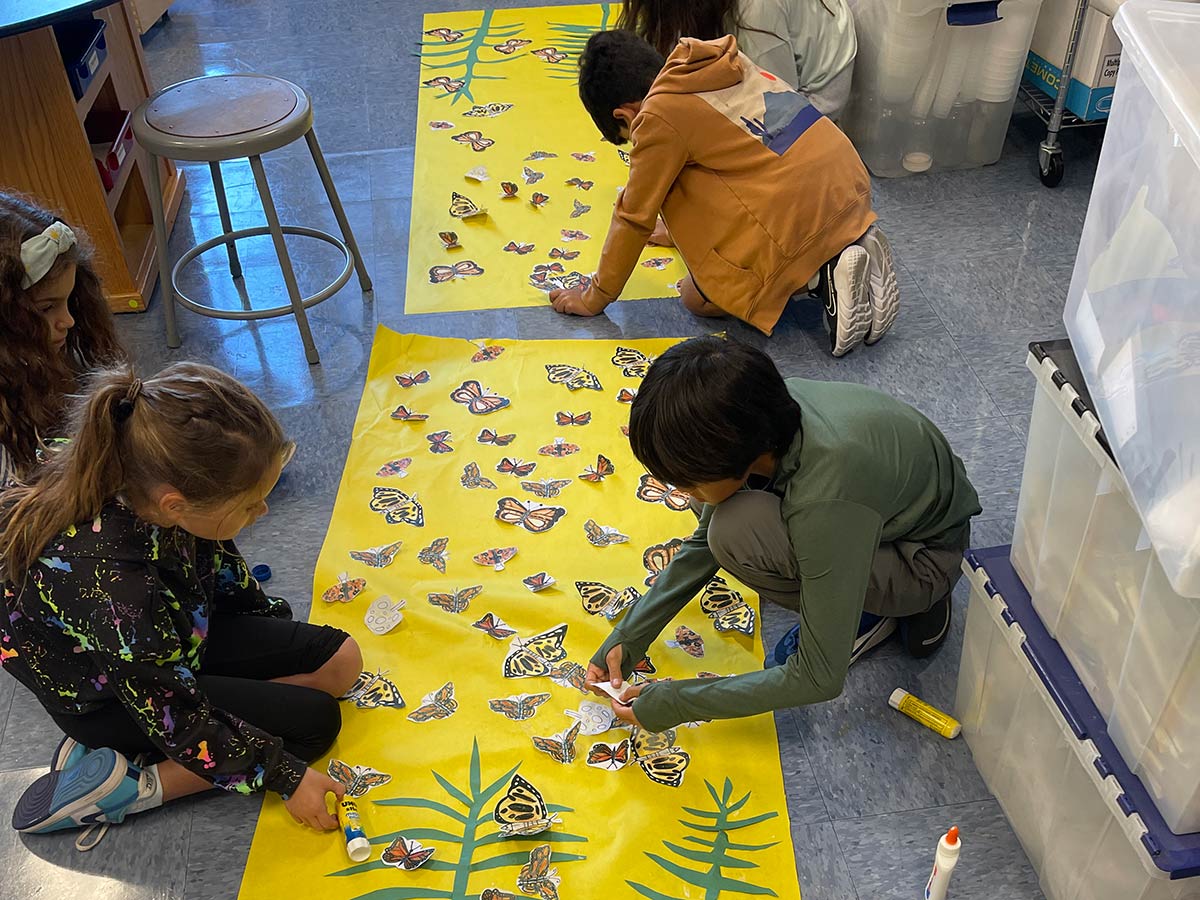 Students on floor working on art with monarch pictures