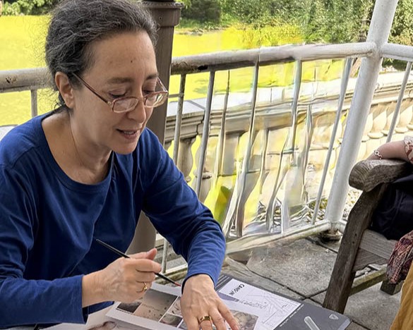 Donna Miskend sits at a table speaking while gesturing to some papers on a table