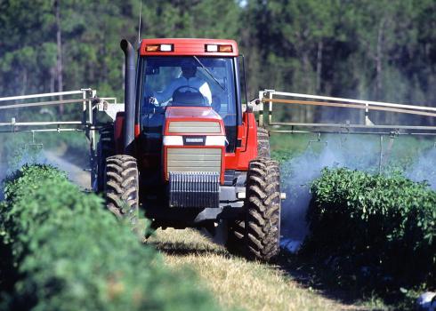 Tractor applying pesticides to rows of crops