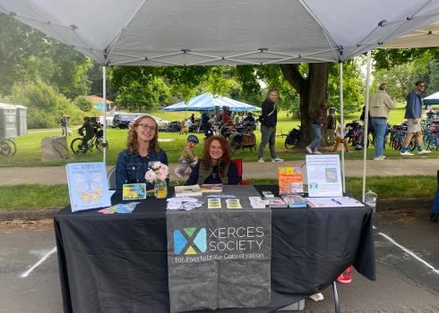 Two women, Sierra Enright and Lisa Loving, sitting behind a Xerces table display at a community event.