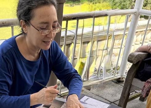 Donna Miskend sits at a table speaking while gesturing to some papers on a table
