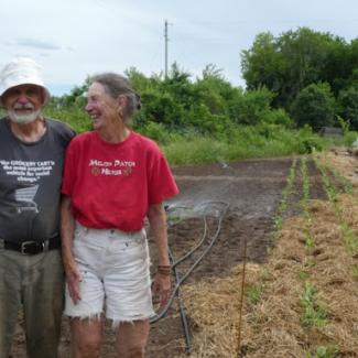 A laughing couple stands in front of several rows of planted seedlings