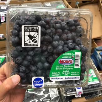 A plastic container of blueberries at a grocery store. The packaging is labeled with the Bee Better Certified seal. 