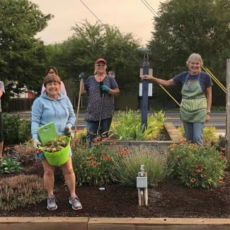 Several Bee City USA participants pose around a flowering garden patch holding garden tools
