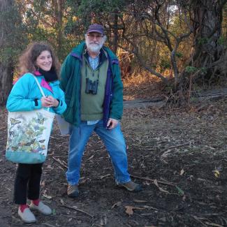 A man and a woman stand nest to each other in front of a grove of old trees.