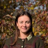 Headshot of woman with brown hair with autumn leaves in background